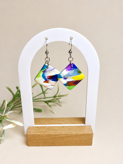 Pendientes Bold de arcilla polimérica en blanco, amarillo, rojo, naranja, verde, azul y purpura sobre expositor