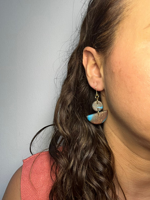 Pendientes Blue Cocoa de arcilla polimérica en marrón y azul puestos en la oreja