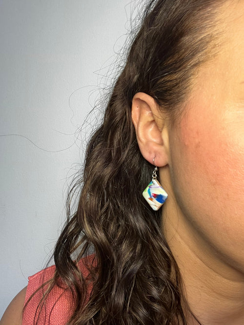 Pendientes Bold de arcilla polimérica en blanco, amarillo, rojo, naranja, verde, azul y purpura puestos en la oreja